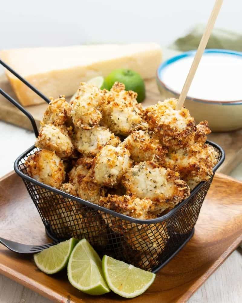 Air fried chicken bites in a frying basket next to some sliced limes