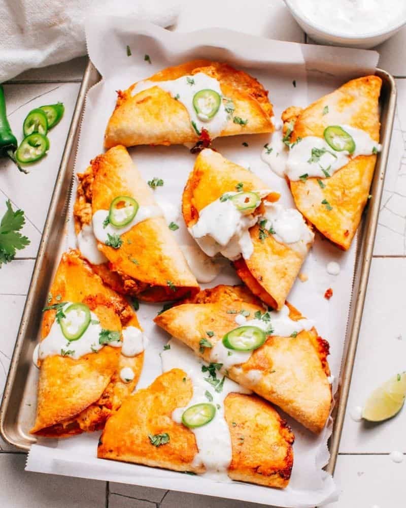 sheet pan with crispy chicken tacos on top with a cream sauce on them