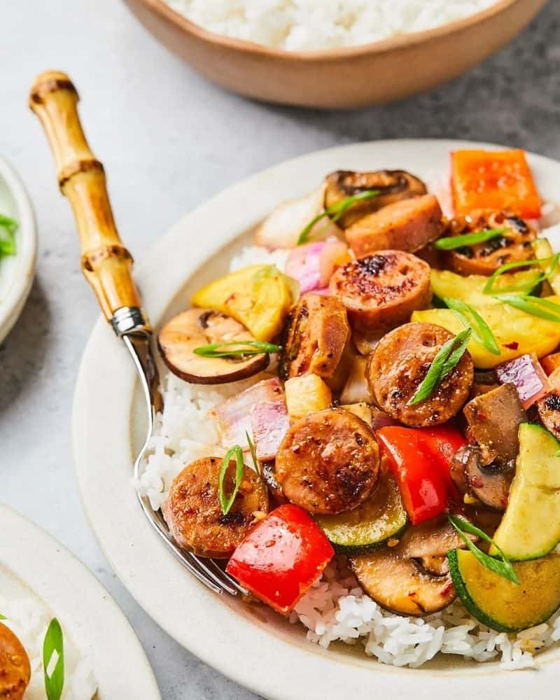 White plate with chicken apple sausage stir fry on top next to a fork