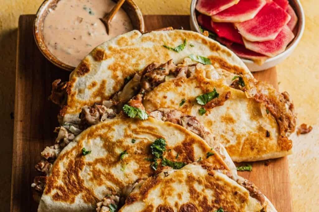 Crispy bean and cheese tacos on a serving board next to dipping sauces