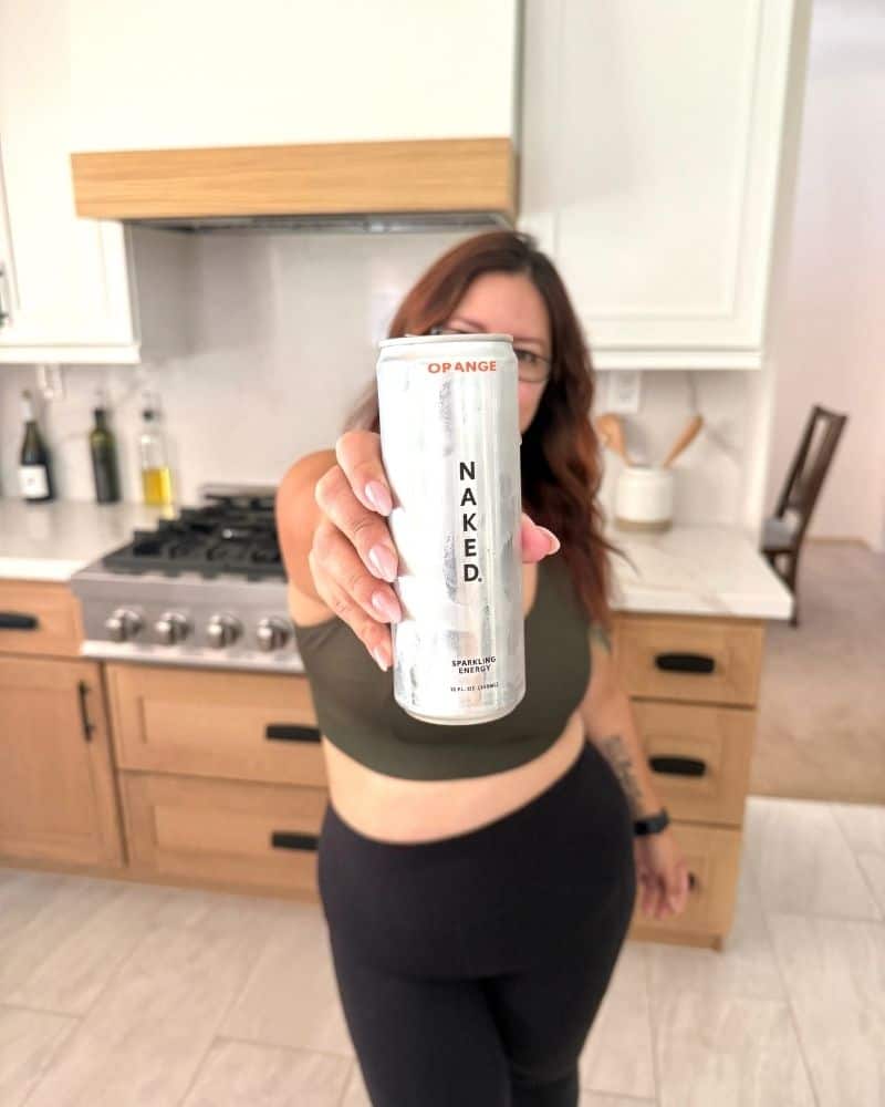 woman in black leggings holding up a Naked Nutrition Energy drink can in the kitchen