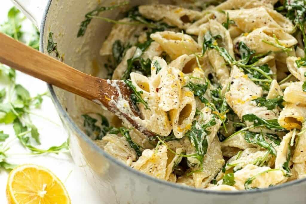 Close up image of a one pot Ricotta Lemon Pasta with a serving spoon in the pot and a lemon half off to the side