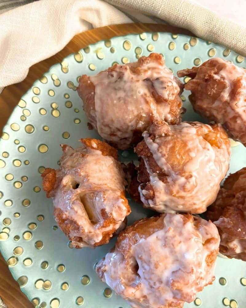 homemade apple fritter balls covered in icing on a green plate
