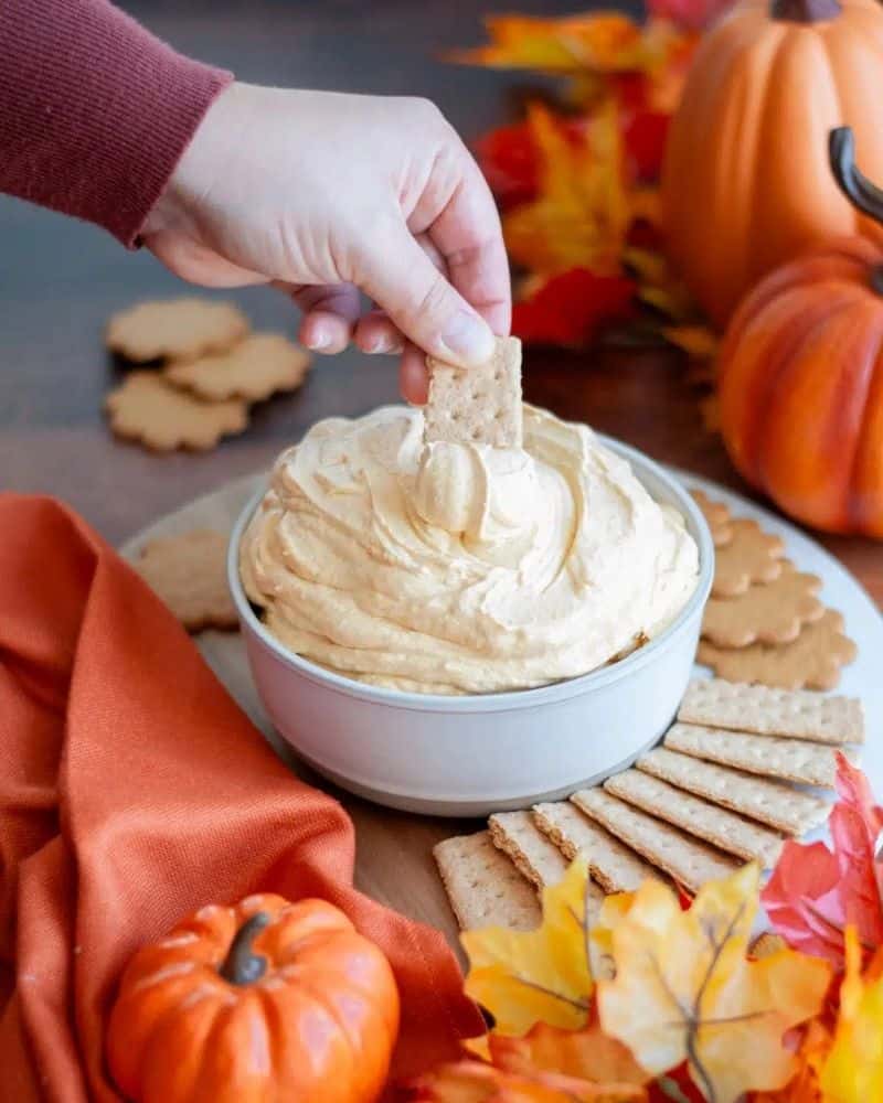 image of a hand dipping a cracker into pumpkin fluff dip